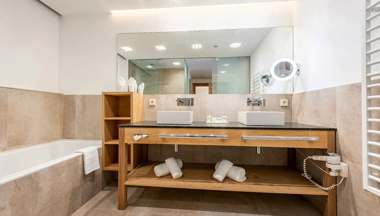 Modern hotel bathroom with wooden vanity, double sinks and beige tile walls