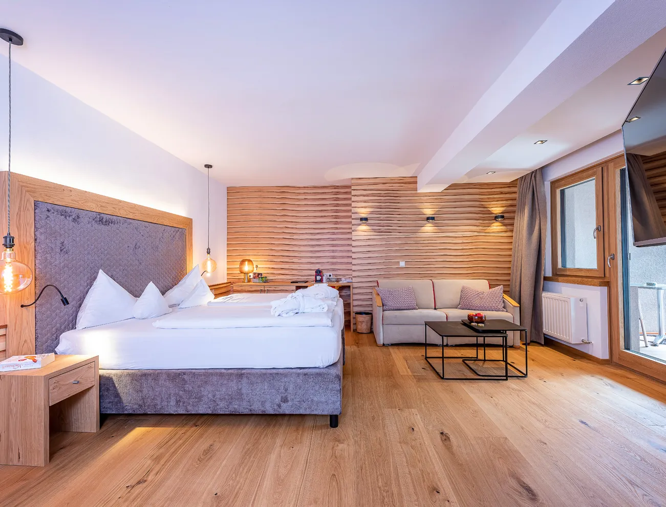 Modernes Hotelzimmer mit Doppelbett, Sofa, Holzakzenten und Zugang zum Balkon