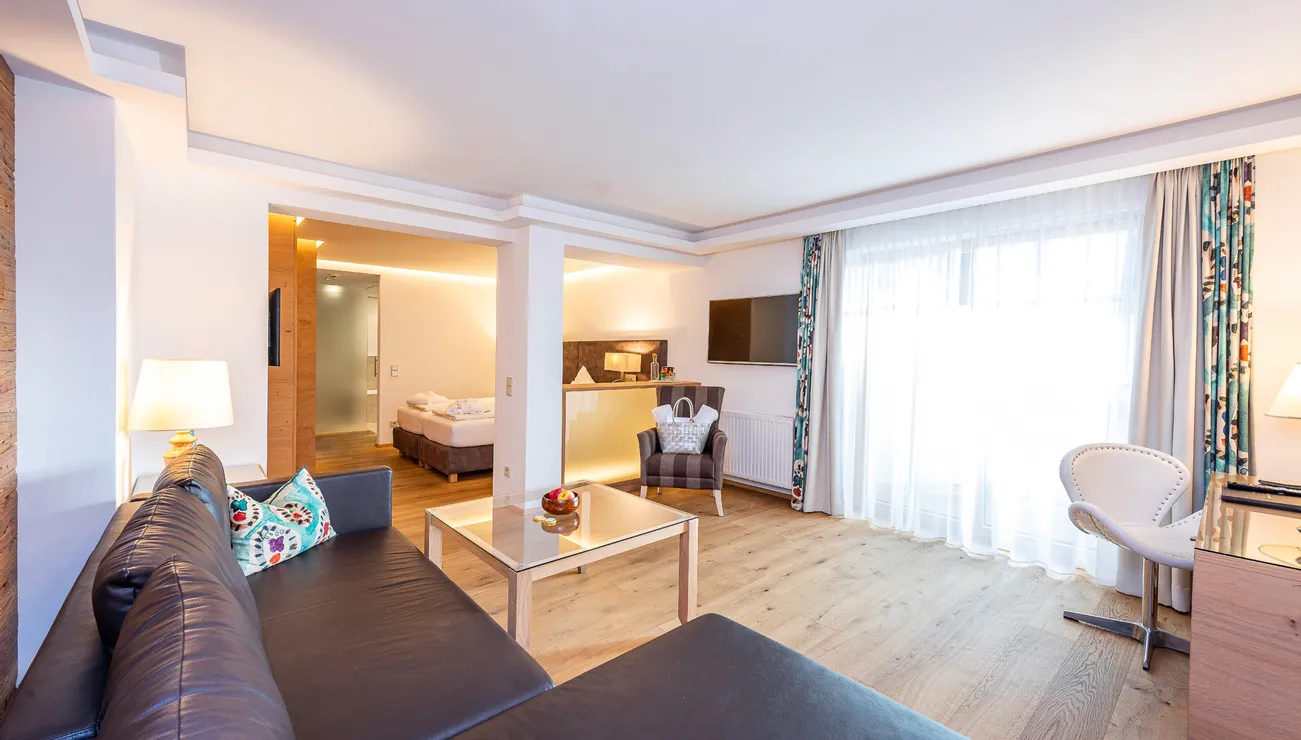 Modern hotel room with wooden floor, seating area, TV and large window with curtains