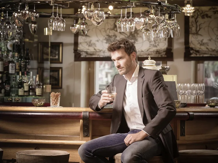 Mann sitzt an der Bar mit einem Glas im Hotel das Neuhaus in Saalbach