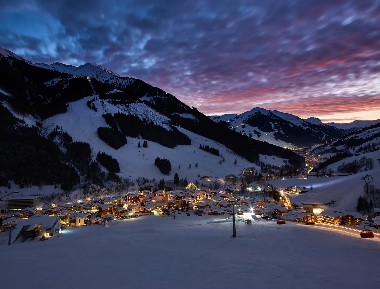 Verschneiter Ort Saalbach Hinterglemm bei Nacht: Atmosphärischer Ausblick für Ihren spontanen Skiurlaub Last Minute.