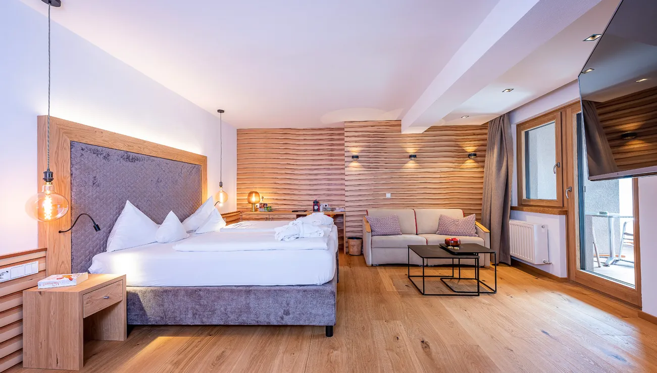 Modern hotel room with double bed, sofa, wood accents and balcony access